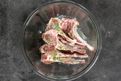 Lamb chops in a bowl with herbs and seasoning.