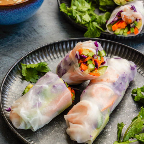 Spring rolls on a plate with herbs and a dipping sauce next to it.