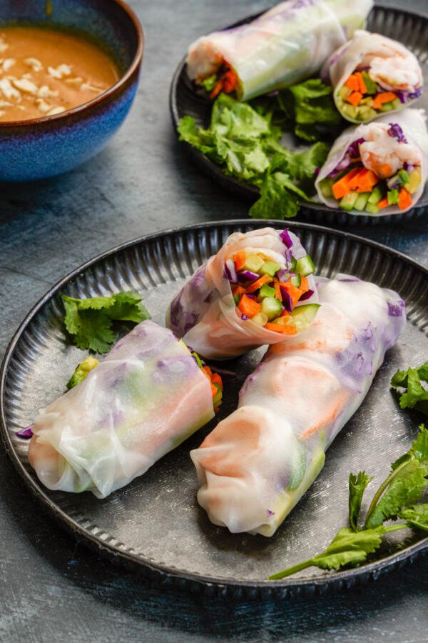 Spring rolls on a plate with herbs and a dipping sauce next to it. 