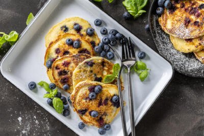 Blueberry pancakes on a plate with utensils and berries.