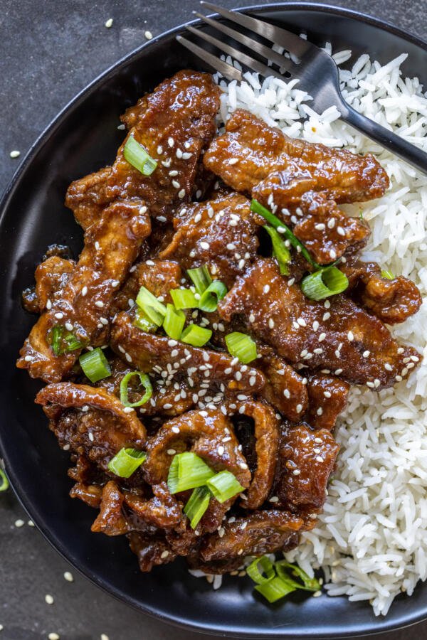 A plate with Mongolian Beef, rice and green onions. 