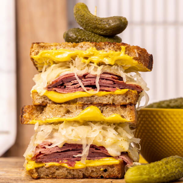 Pastrami Sandwich on a board with pickles next to it.