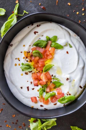 Creamy cottage cheese with herbs and tomato on a bowl.