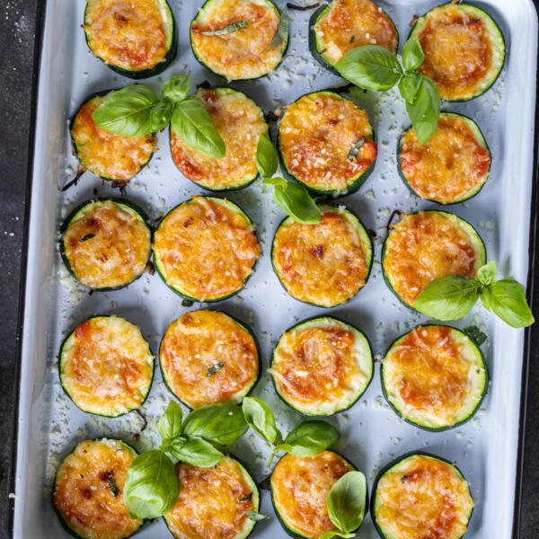 Baked Zucchini Pizza Bites on a baking sheet with herbs around.