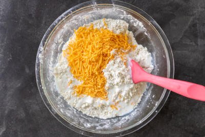 Shredded cheddar cheese added to the remainder biscuits ingredients in a bowl.