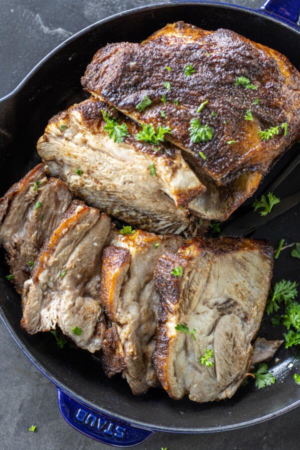 Sliced pork roast on a pan with herbs.
