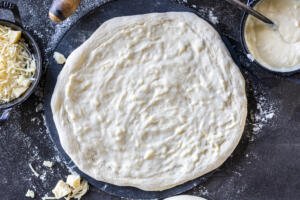 Spread out pizza dough with pizza sauce on it.