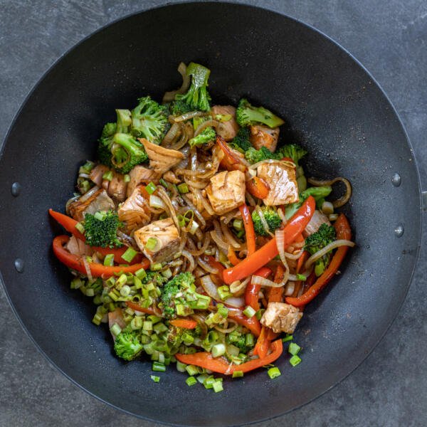 Veggies with sauce added to salmon in a wok.