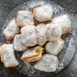 Beignets with powder sugar on a serving tray.