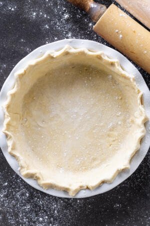 Pie crust in a pan with flour around.