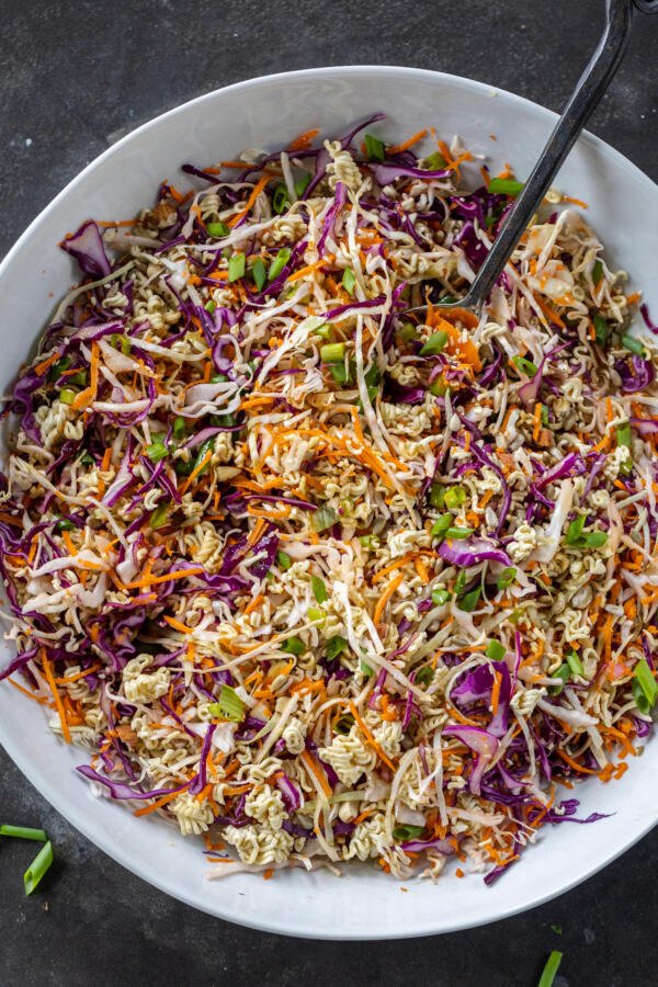 Ramen Noodle Salad in a bowl with a spoon and dressing added. 