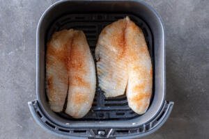 Seasoned tilapia in air fryer basket.