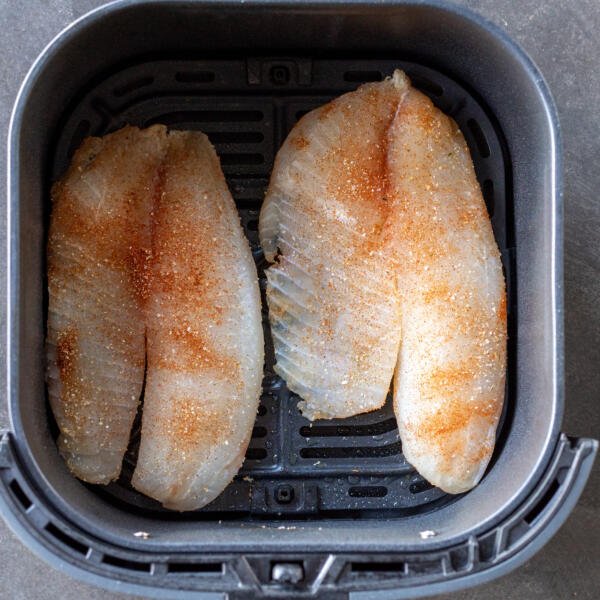 Seasoned tilapia in air fryer basket.