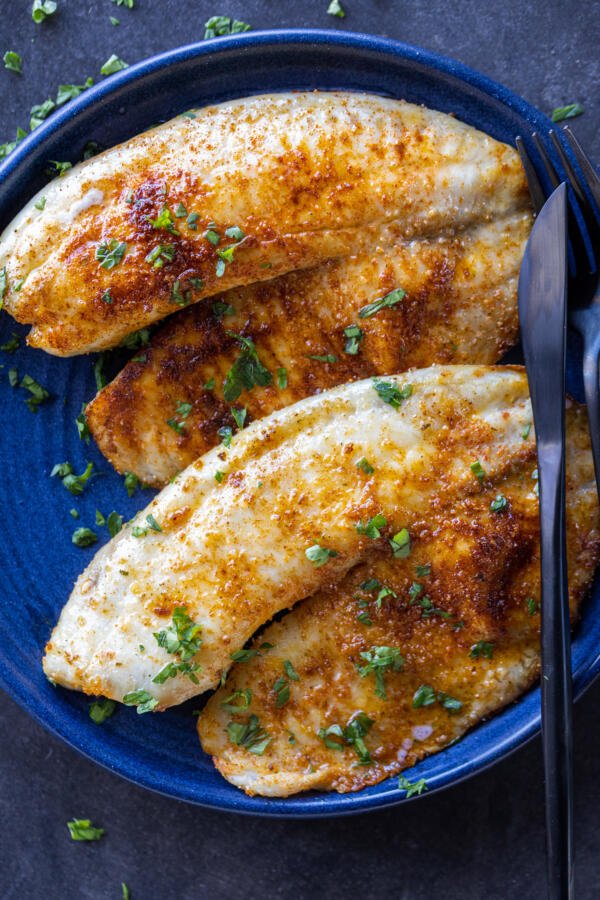 Air Fryer Tilapia on a plate with herbs.