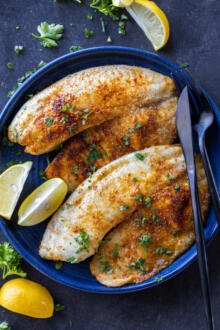 Air Fryer Tilapia on a plate with herbs and lemon.