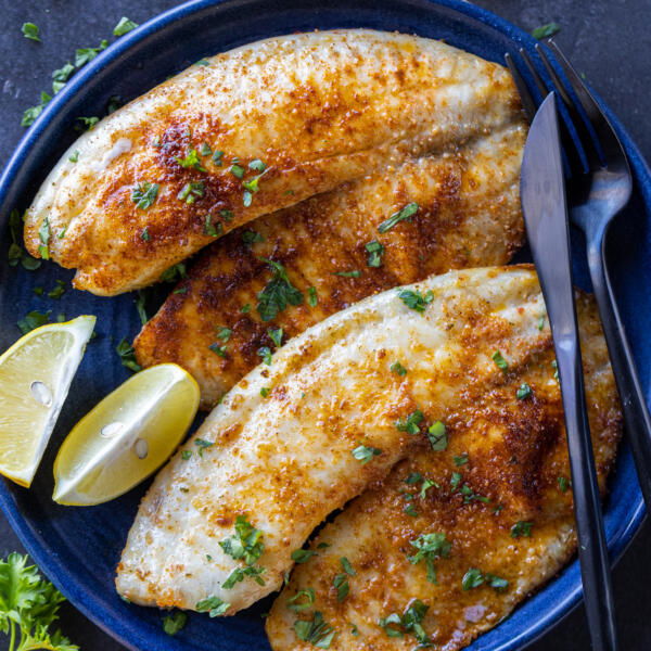 Air Fryer Tilapia on a plate with herbs and lemon.