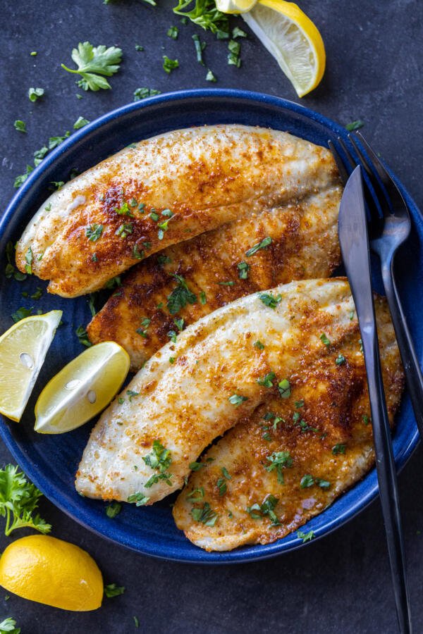Air Fryer Tilapia on a plate with herbs and lemon. 