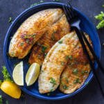 Air Fryer Tilapia on a plate and herbs with lemon.