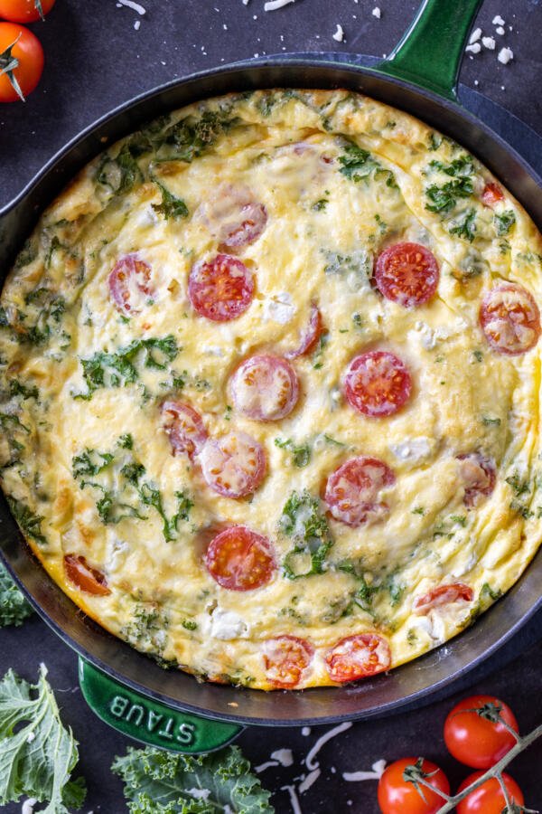 Frittata in a pan with tomatoes next to it.