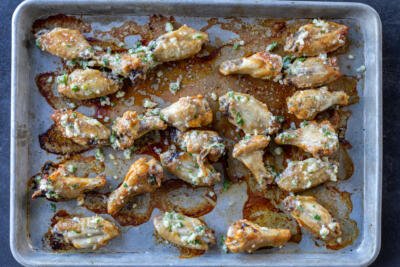 A baking pan with baked wings and parmesan toppings.