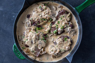 Steak in a pan with creamy sauce and herbs.