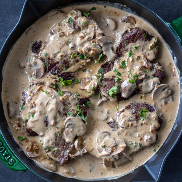 Steak in a pan with creamy sauce and herbs.