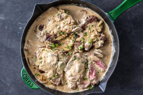 Steak in mushrooms sauce in a pan with herbs.
