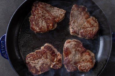 Frying pan with steak frying in it.