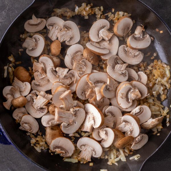 Onions in a frying pan with mushrooms added to the pan.