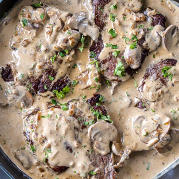 Creamy sauce over steak in a pan.
