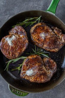 Filet Mignon on a frying pan with butter and herbs.