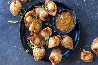 Fried Wontons on a serving tray with sauce and herbs.