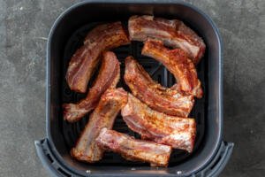 Seasoned ribs in an air fryer basket.