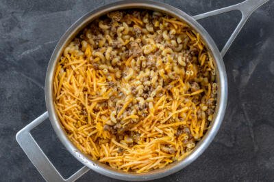 Cheese added to the pasta and beef in a pan.