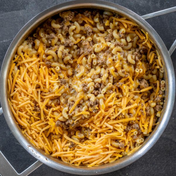 Cheese added to the pasta and beef in a pan.