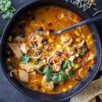 Chicken Enchilada Soup in a bowl with chips and herbs.