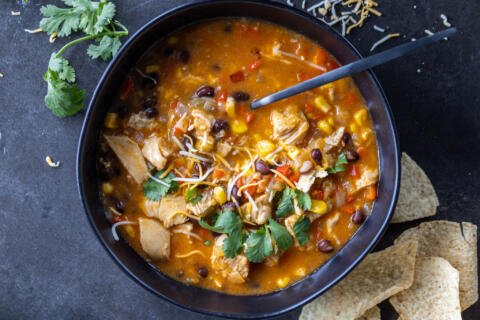 Chicken Enchilada Soup in a bowl with chips and herbs.