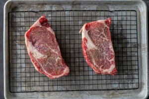 Seasoned steak on a wire baking rack.