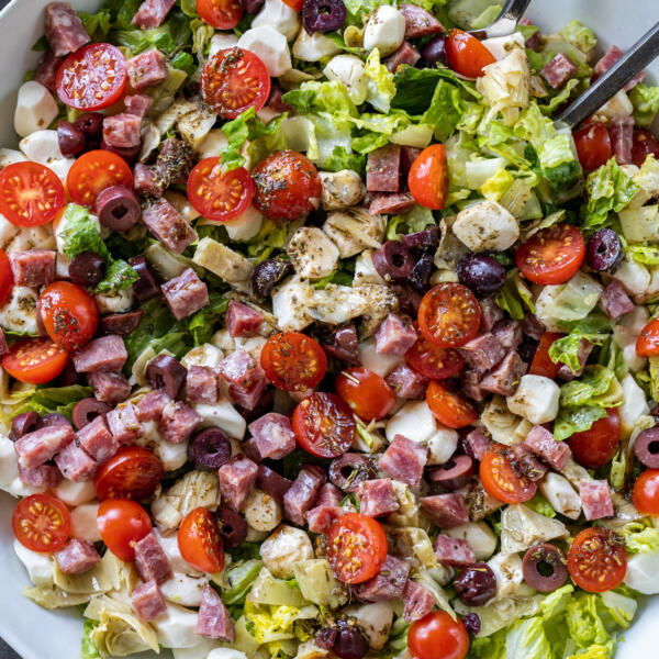 Antipasto Salad & Dressing with serving utensils.
