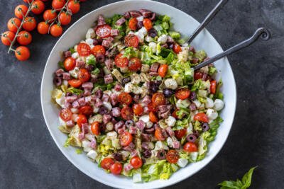 Antipasto Salad with Dressing and serving utensils.