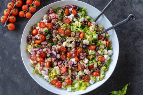 Antipasto Salad with Dressing and serving utensils.