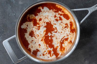 Cream added to tomato sauce in a pan.