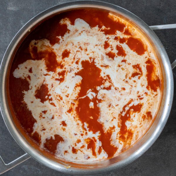 Cream added to tomato sauce in a pan.