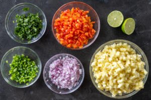 Chopped veggies and herbs in bowls with lime next to it.