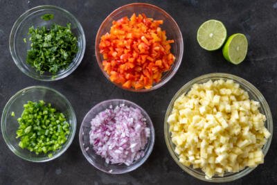 Chopped veggies and herbs in bowls with lime next to it.