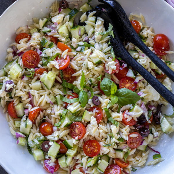 Serving bowl with utensils and Greek Orzo Salad with Feta.