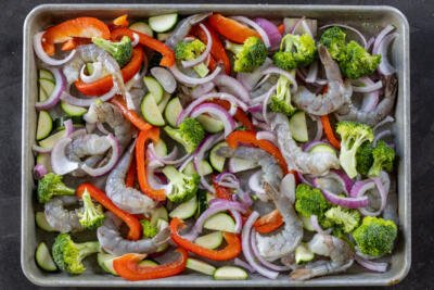 Sheet pan with veggies and raw shrimp on a pan with seasoning.