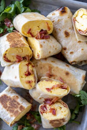 Bacon Egg And Cheese Burritos with herbs and bacon next to it.