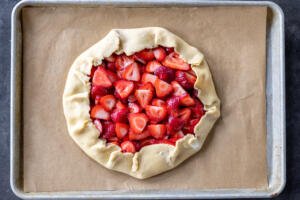 Shaped galette with strawberries on a baking sheet.