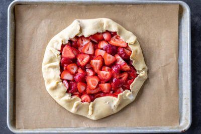 Shaped galette with strawberries on a baking sheet.